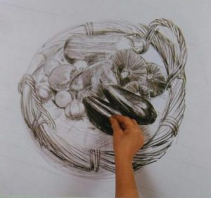 hand adding finishing touches to the drawing of a basket with vegetables