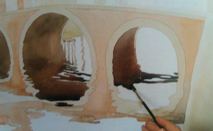 paitbrush adding details to a bridge on the water on a painting made with watercolors