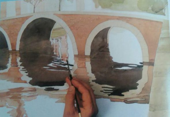 hand with the paintbrush adding finishing details to a painting of a bridge made with watercolors