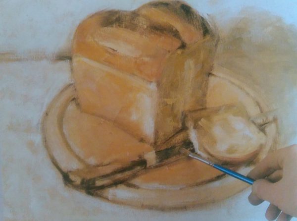hand with a brushes addingfinal details to the painting of a bread and knife on a cutting board 