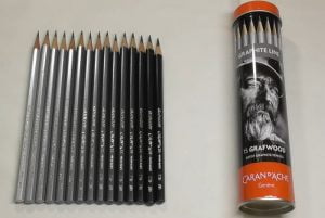 Metal box of Caran D'ache graphite pencils next to several pencils neatly aligned on a white surface