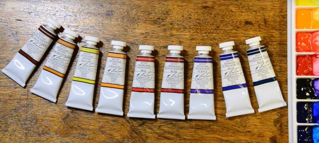 several tubes of M.Graham watercolors aligned on the desk