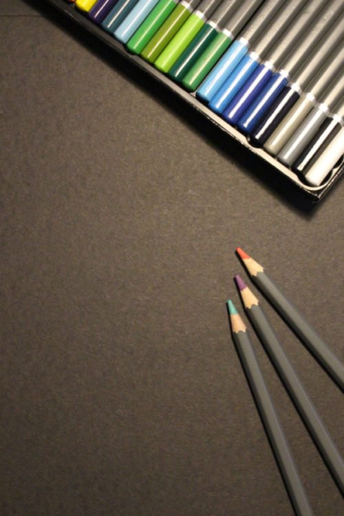 several pencils next to an open box of colored pencils on a brownish grey surface