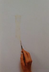 hand with a paintbrush starting to sketch a lighthouse on a white surface